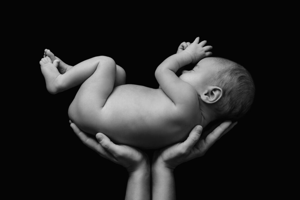 A black and white image of two hands holding a baby