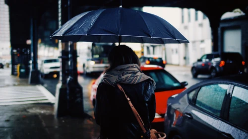 A city scape in rain focusing on a woman carrying an umbrella